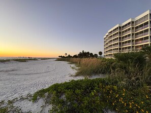 A beachfront hotel with multiple balconies, a sandy beach, and a clear sky.