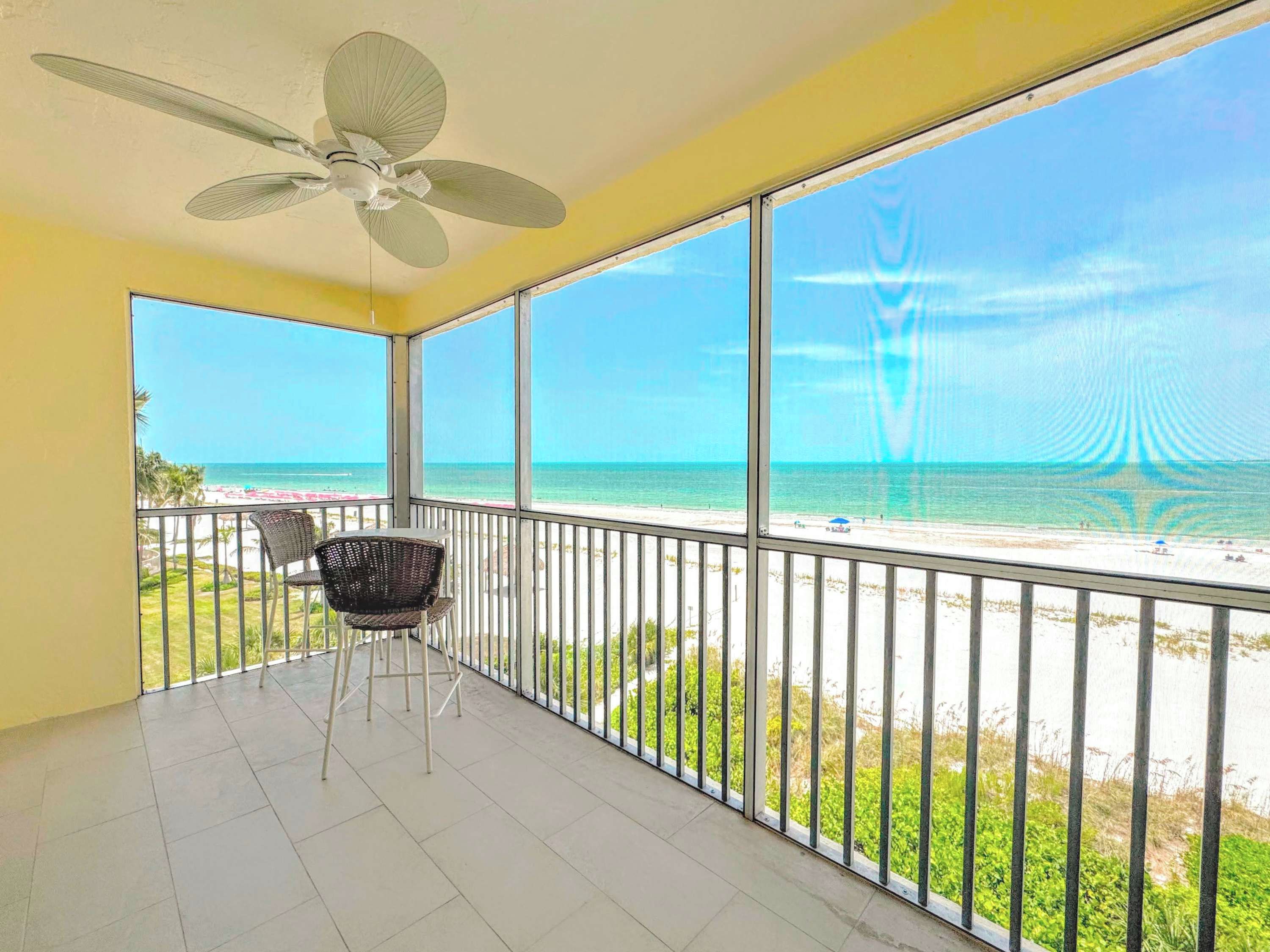 Un balcon doté d’un ventilateur de plafond, d’une chaise et offrant une vue sur la plage.