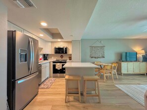 A modern kitchen with a refrigerator, microwave, and stove. There is a dining area with a table and chairs. - Vacation Villas #432 - Beachfront Condo (Fort Myers Beach)