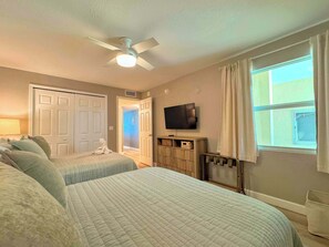 A hotel room with two beds, a ceiling fan, a television, and a window with curtains.