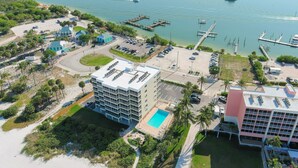 An aerial view of a coastal hotel with a swimming pool, parking area, and marina with boats.