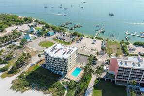 An aerial view of a coastal hotel with a swimming pool, parking area, and marina with boats.