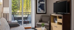A modern living room with a sofa, armchair, television, and a potted plant. - Charming 1-bedroom condo in peaceful Canmore with fitness room (Canmore)