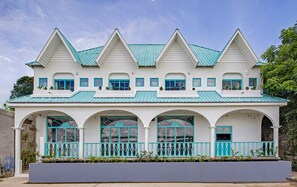 Een gebouw met twee verdiepingen, een witte gevel, blauwe decoratielijsten en een groen dak.