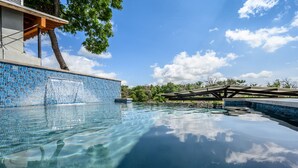 Ein klares Schwimmbecken mit einer gefliesten Kante, einer Holzterrasse und einem Baum im Hintergrund.