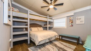 Ein Schlafzimmer mit Etagenbett, Deckenventilator, Fenster mit Jalousien, einer Bank und einem Teppich.