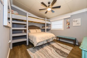 Ein Schlafzimmer mit Etagenbett, Deckenventilator, Fenster mit Jalousien, einer Bank und einem Teppich.