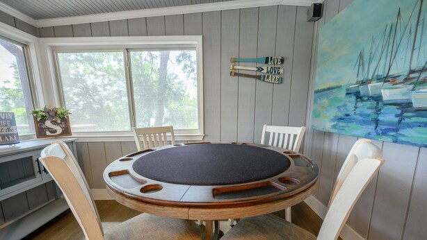 Ein runder Holztisch mit gepolsterten Stühlen in einem Raum, dessen Wände mit Holz verkleidet sind, mit einem Segelbootgemälde und einem Willkommensschild.