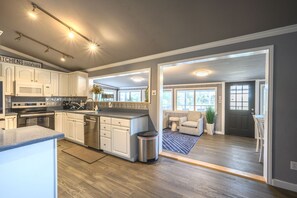 A modern kitchen with white cabinets, stainless steel appliances, and a large window.