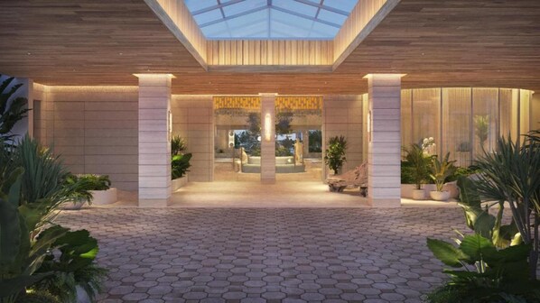 A modern building entrance with a glass ceiling, hexagonal paving, and potted plants.