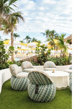 Outdoor seating with round tables and cushioned chairs, surrounded by greenery and umbrellas.
