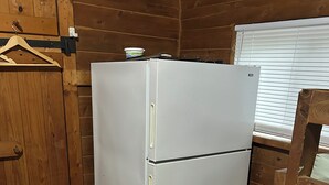 A compact kitchen with a white refrigerator, wooden walls, and a window with blinds. - Sun Outdoors Sarasota (Sarasota)