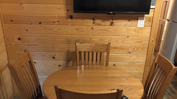 A wooden-paneled room with a round table and four chairs, a flat-screen TV mounted on the wall, and a refrigerator in the background. - Sun Outdoors Sarasota (Sarasota)