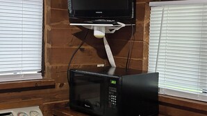 A room with a wooden wall, a black microwave, a black television on a stand, and a white air conditioning unit. - Sun Outdoors Sarasota (Sarasota)
