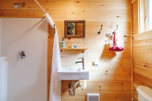 A wooden cabin bathroom with a white sink, a shower curtain, a mirror, and a towel rack. - 6 Private Cabins for Groups + Sauna + Walk to Sandy Point Beach (Stockton Springs)