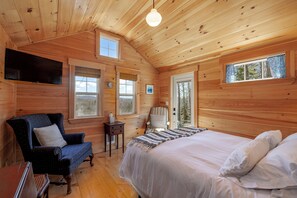 A wooden cabin room with a bed, a chair, a television, and a window. - 6 Private Cabins for Groups + Sauna + Walk to Sandy Point Beach (Stockton Springs)
