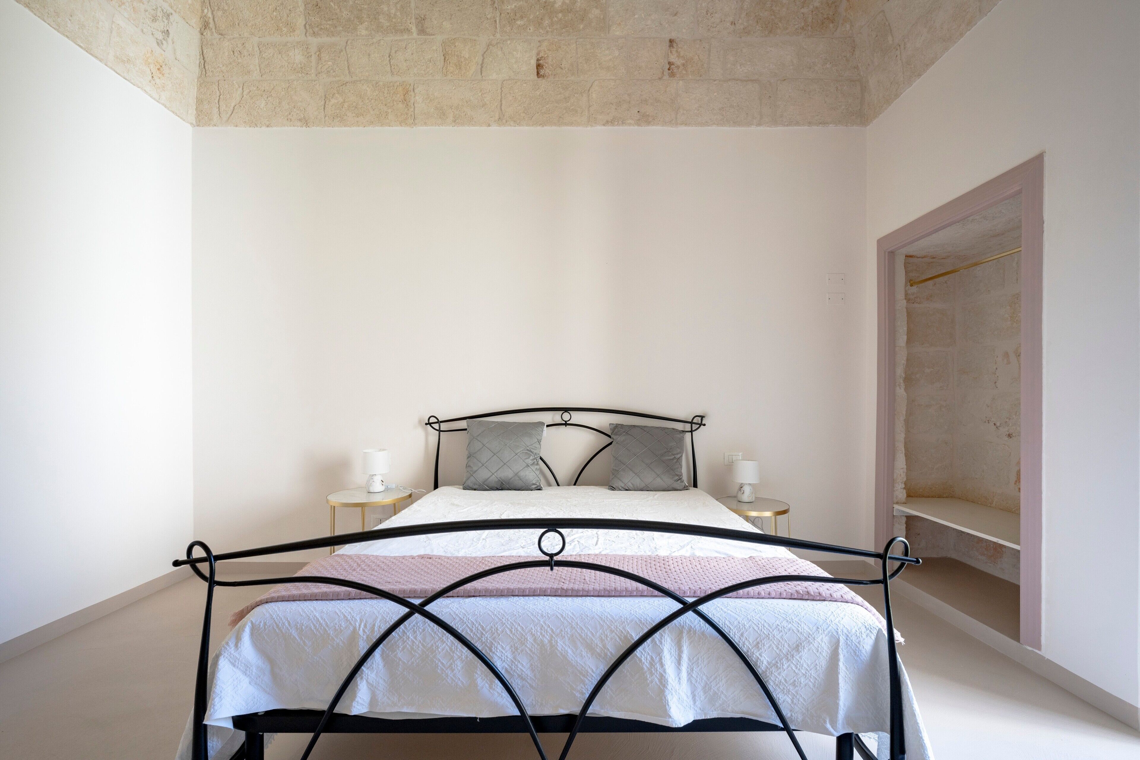 Un lit simple avec un cadre en métal, deux tables de chevet avec des lampes et un mur sobre agrémenté d’un élément décoratif en pierre.