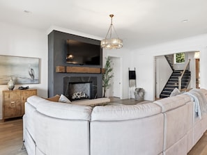 A modern living room with a sectional sofa, a fireplace, and a staircase leading to another level.