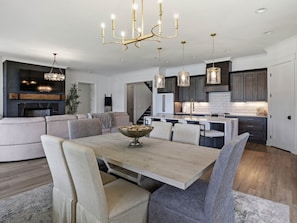 Een moderne keuken met een centraal eiland, hangende lampen en een eethoek met een houten tafel en gestoffeerde stoelen.