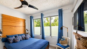 A bedroom with a bed, a desk, a chair, a window with curtains, and a ceiling fan. - Cliffside Caribbean Condo: Beach & Ocean Views (Ocho Rios)