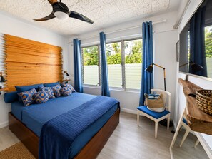 Ein Schlafzimmer mit einem Bett, einem Schreibtisch, einem Stuhl, einem Fenster mit Vorhängen und einem Deckenventilator.