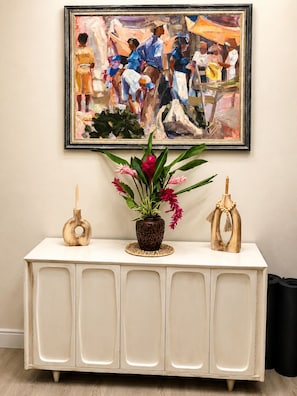 A white console table with a vase of flowers, a wooden sculpture, and a framed painting above.