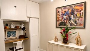 A room with a white desk, a framed painting, a console table with decorative items, and a woven rug. - Cliffside Caribbean Condo: Beach & Ocean Views (Ocho Rios)