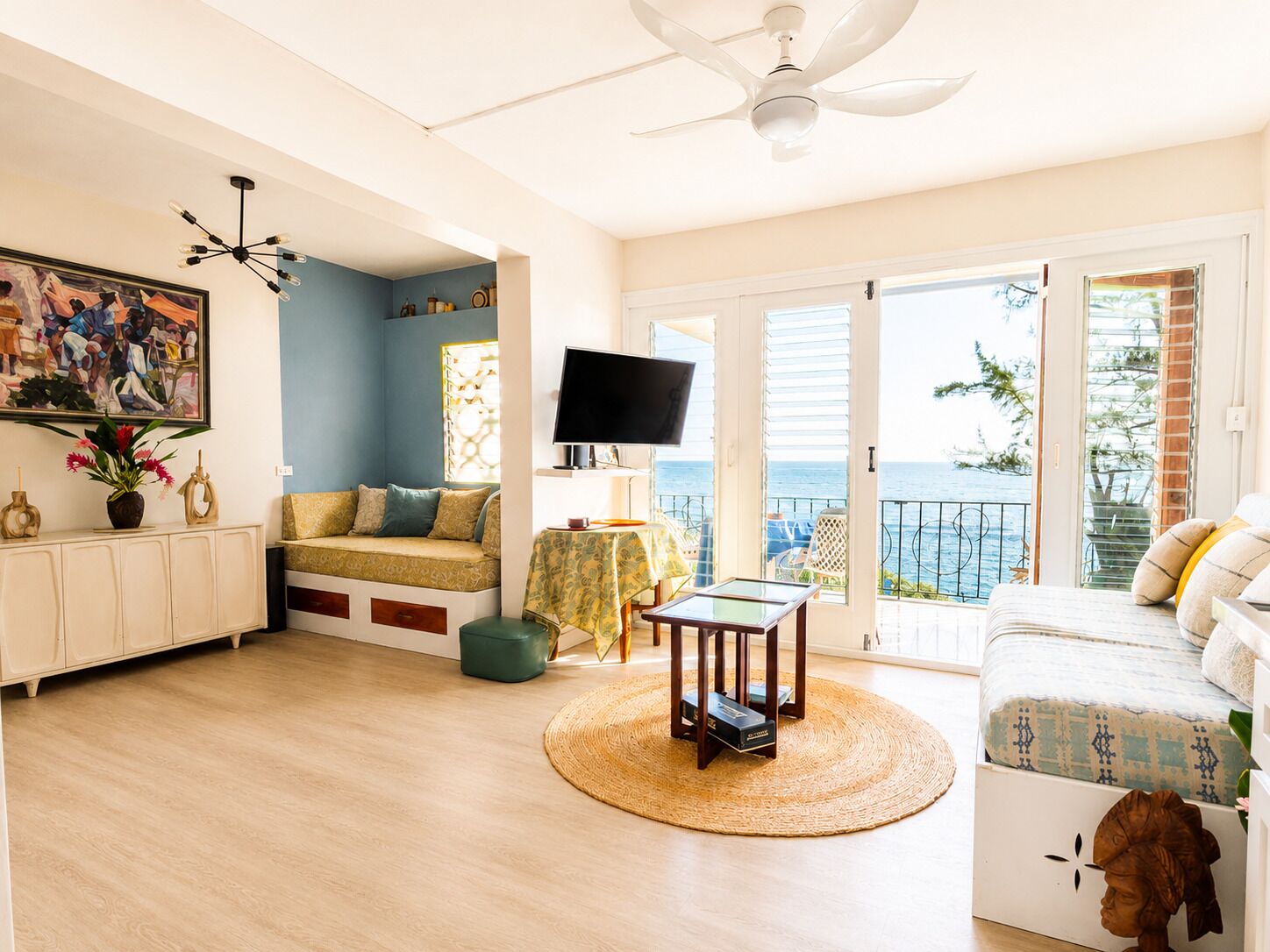 Sala de estar com sofá, televisão, ventilador de teto e vista para o mar.