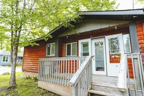A wooden cabin with a porch, a set of stairs, and a door with a window. - Heron Cottage - 3-Bedroom Cottage – Family Friendly (Trent Lakes)