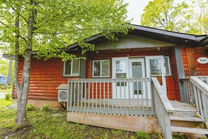 En stuga byggd av trä med en veranda, en inglasad uteplats och en liten luftkonditioneringsanläggning.