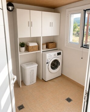 A laundry room with a washing machine, a drying rack, and storage cabinets. - Family Olive Grove Retreat. (Petras)