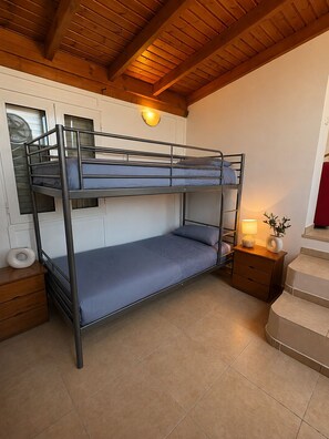 A bunk bed room with a wooden ceiling, a nightstand with a lamp, and a window with blinds. - Family Olive Grove Retreat. (Petras)
