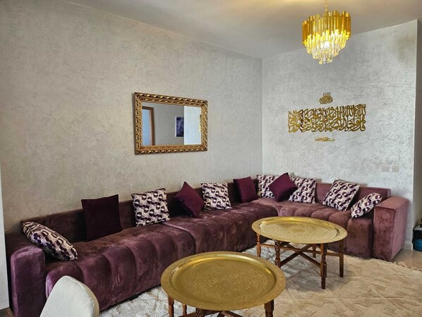A living room with a sofa, two round coffee tables, a chandelier, a mirror, and decorative wall art.