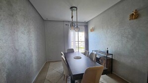 Ein Essbereich mit einem langen Tisch, Stühlen, einer Chandelüster und einem Fenster mit Vorhängen.