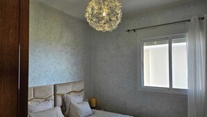 Ein Schlafzimmer mit einem Bett, einer Kristallleuchtre, einem Fenster mit Vorhängen und einer strukturierten Wand.