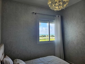 A bedroom with a large window, a bed, and a chandelier.