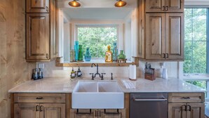 A kitchen with wooden cabinets, a double sink, and a window with a view of greenery.
