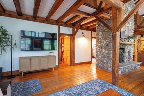 A spacious room with wooden beams, a stone wall, a fireplace, and a large flat-screen TV. - Tranquil Manor - Lake Geneva English Tudor Estate (Lake Geneva)