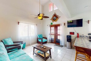Ein Wohnzimmer mit Sofa, Couchtisch, Deckenventilator, Fernseher und Wasserspender.