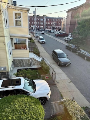 Une rue résidentielle bordée de voitures garées et un immeuble à deux étages doté d’un balcon.