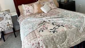 A neatly made bed with floral bedding, a headboard, a bedside table with a lamp, and a wall-mounted picture.