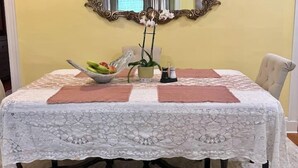 A dining table with a lace tablecloth, a decorative mirror above it, and a floral centerpiece.