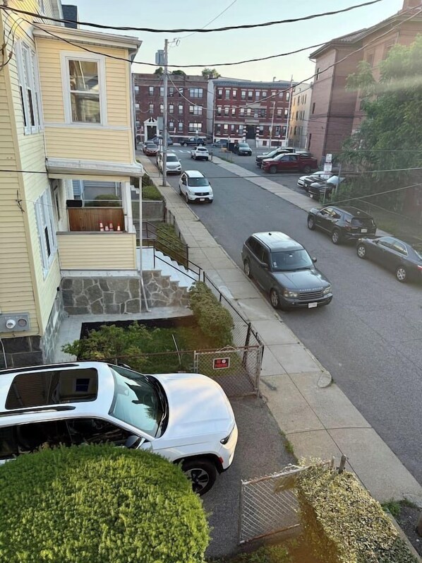 A residential street with parked cars and a two-story building with a balcony.