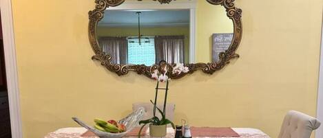A dining table with a lace tablecloth, a decorative mirror above it, and a vase with flowers on the table.