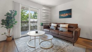 A living room with a brown leather sofa, a round coffee table, a potted plant, and a cityscape painting on the wall. - UW Hospital Retreat with Dedicated Workspace (Madison)