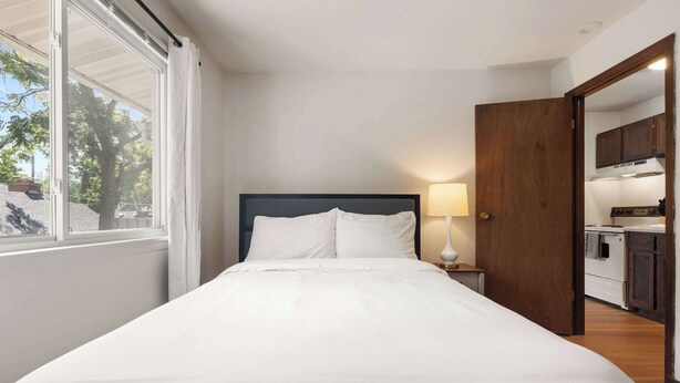 A bedroom with a bed, a nightstand, a lamp, and a view of the outdoors. - UW Hospital Retreat with Dedicated Workspace (Madison)