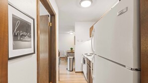 A narrow hallway leading to a kitchen with a refrigerator, a trash bin, and a dining area with a table and chairs. - UW Hospital Retreat with Dedicated Workspace (Madison)