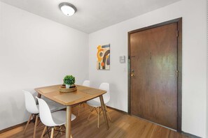 Ein Zimmer mit Holztisch, weißen Stühlen, einer Topfpflanze und einer Tür.