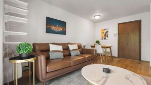 A modern living room with a brown leather sofa, a round marble coffee table, and a cityscape painting on the wall. - UW Hospital Retreat with Dedicated Workspace (Madison)