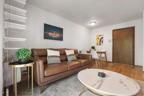 A modern living room with a brown leather sofa, a round marble coffee table, and a cityscape painting on the wall.